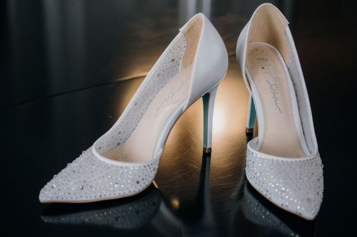 Free Elegant white high heels adorned with rhinestones, reflecting soft light on a glossy surface. Stock Photo