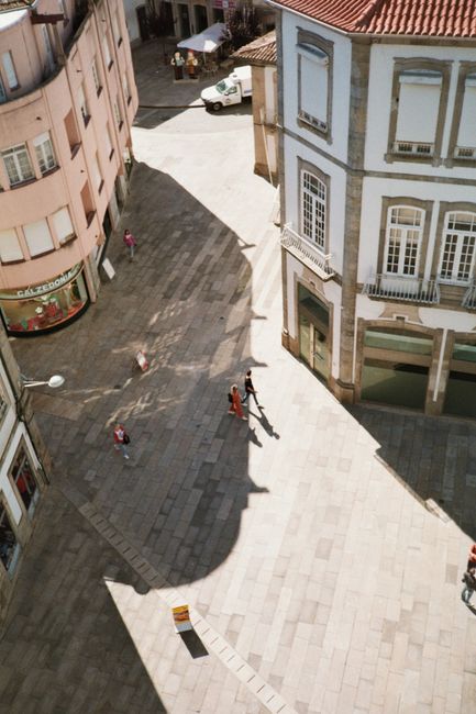 Aerial view of a sunny European street with people walking past historic buildings.
