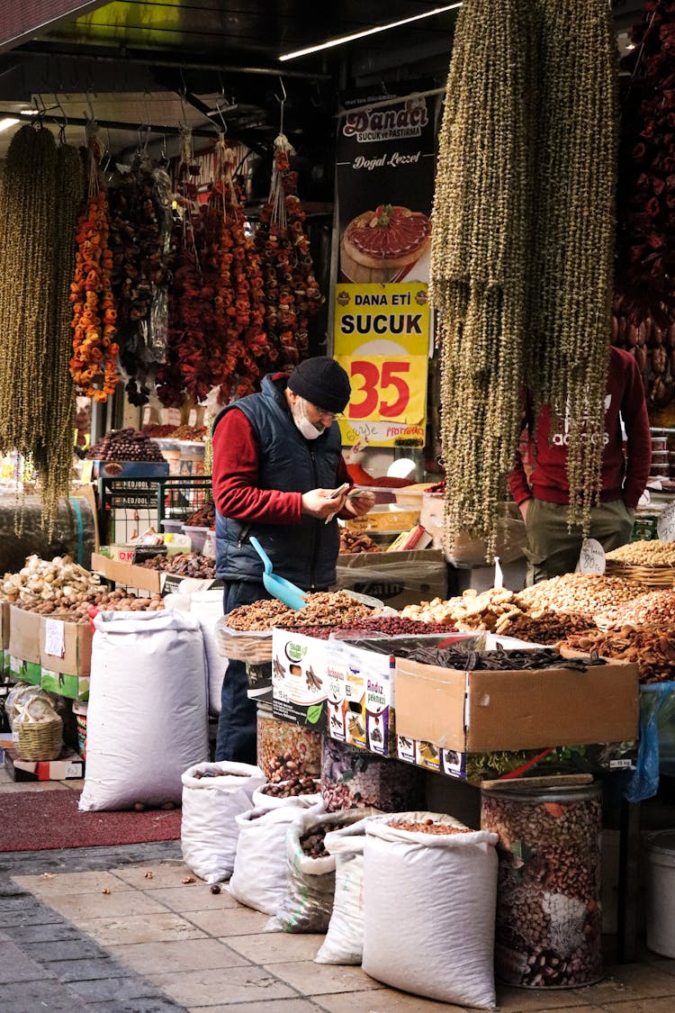 Man In Red Long Sleeve Shirt And Black Vest Buying On A Store In Marketplace