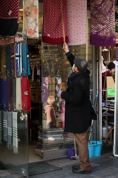 A vendor adjusting vibrant scarves hanging outside a shop in a bustling marketplace.