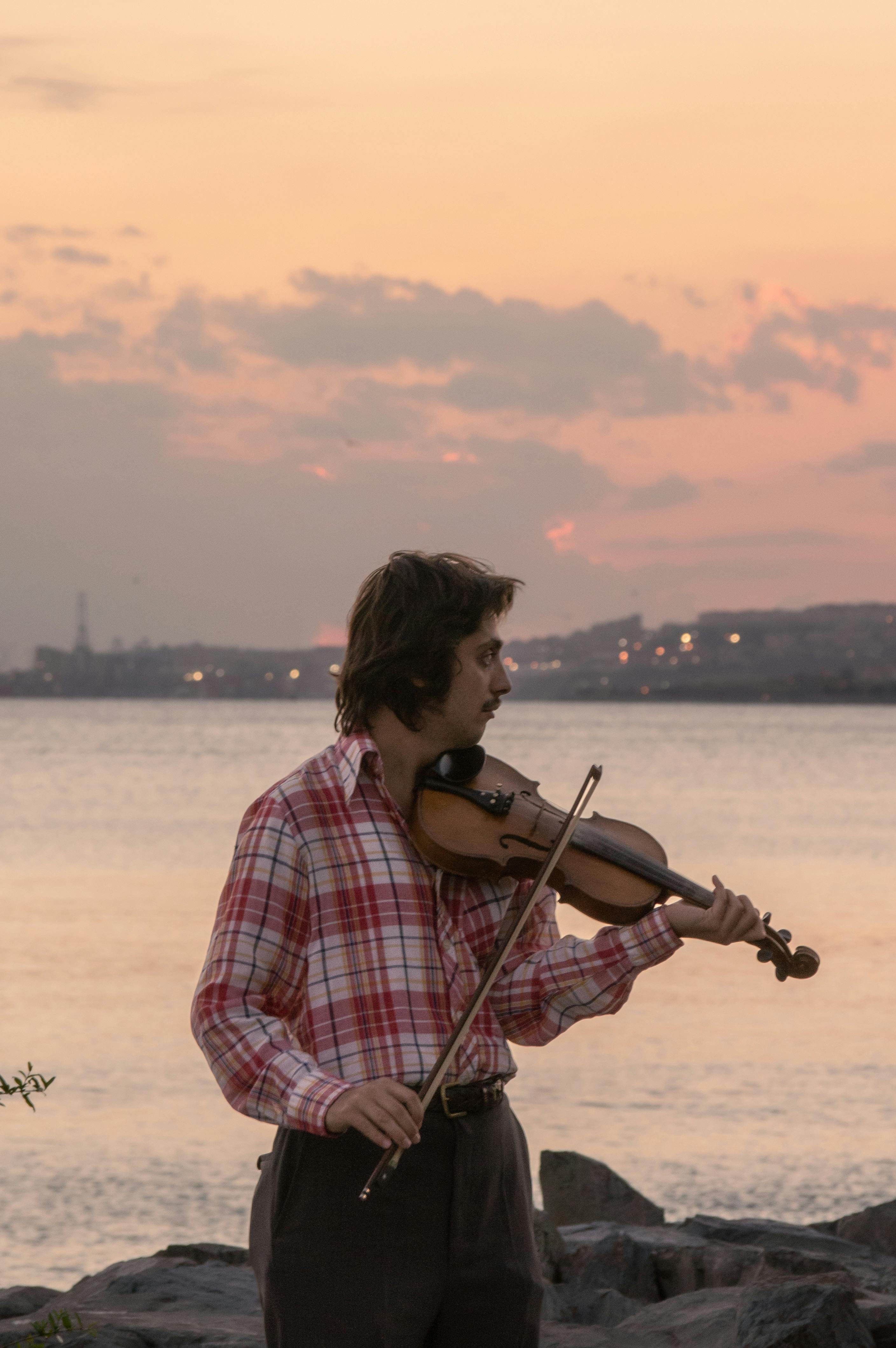 Musician in İstanbul playing violin at sunset by the water. Captivating evening atmosphere.