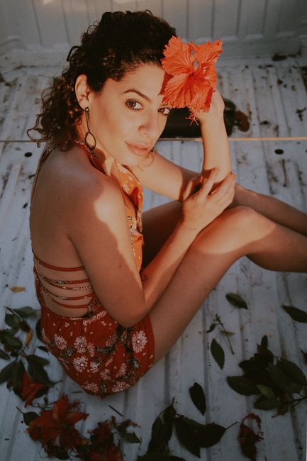 Portrait of a woman sitting outdoors with a hibiscus flower in her hair, evoking a warm and vibrant mood.