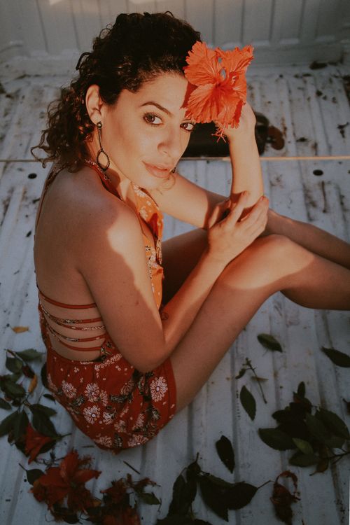 Free Portrait of a woman sitting outdoors with a hibiscus flower in her hair, evoking a warm and vibrant mood. Stock Photo
