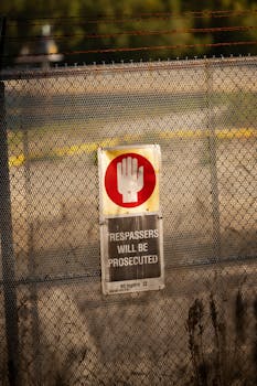 Close-up of a warning sign on a chain link fence cautioning trespassers with legal action.