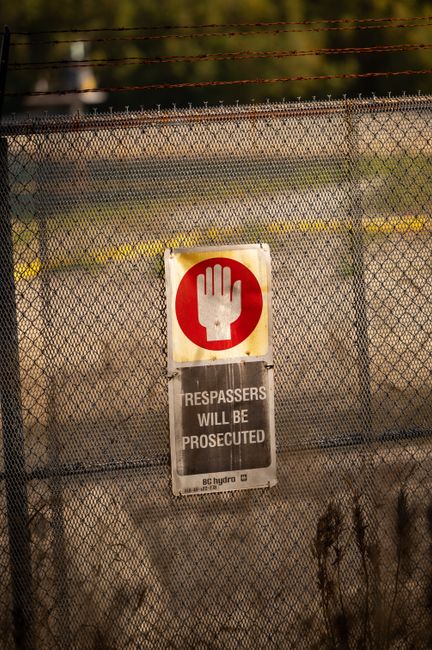 Close-up of a warning sign on a chain link fence cautioning trespassers with legal action.