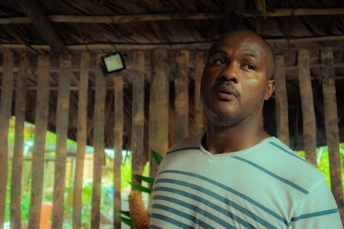 Man in Blue and White Striped Crew Neck Shirt Standing Near Wooden Fence