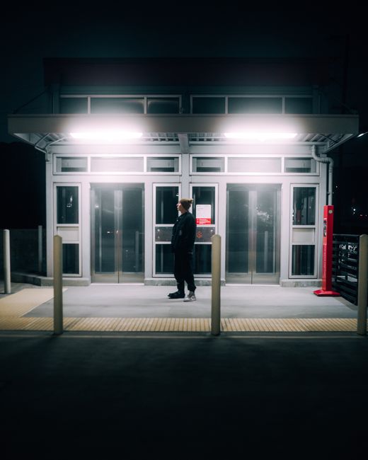 Person stands at night on a lit platform in Los Angeles with elevators and bright overhead lights.