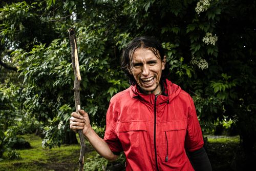 Free A man in a vibrant red jacket holding a stick, smiling in a Bogotá park. Stock Photo