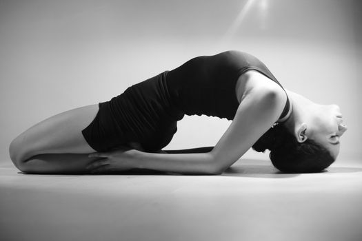 Monochrome photo of a woman performing a yoga pose, demonstrating flexibility and grace in a studio.