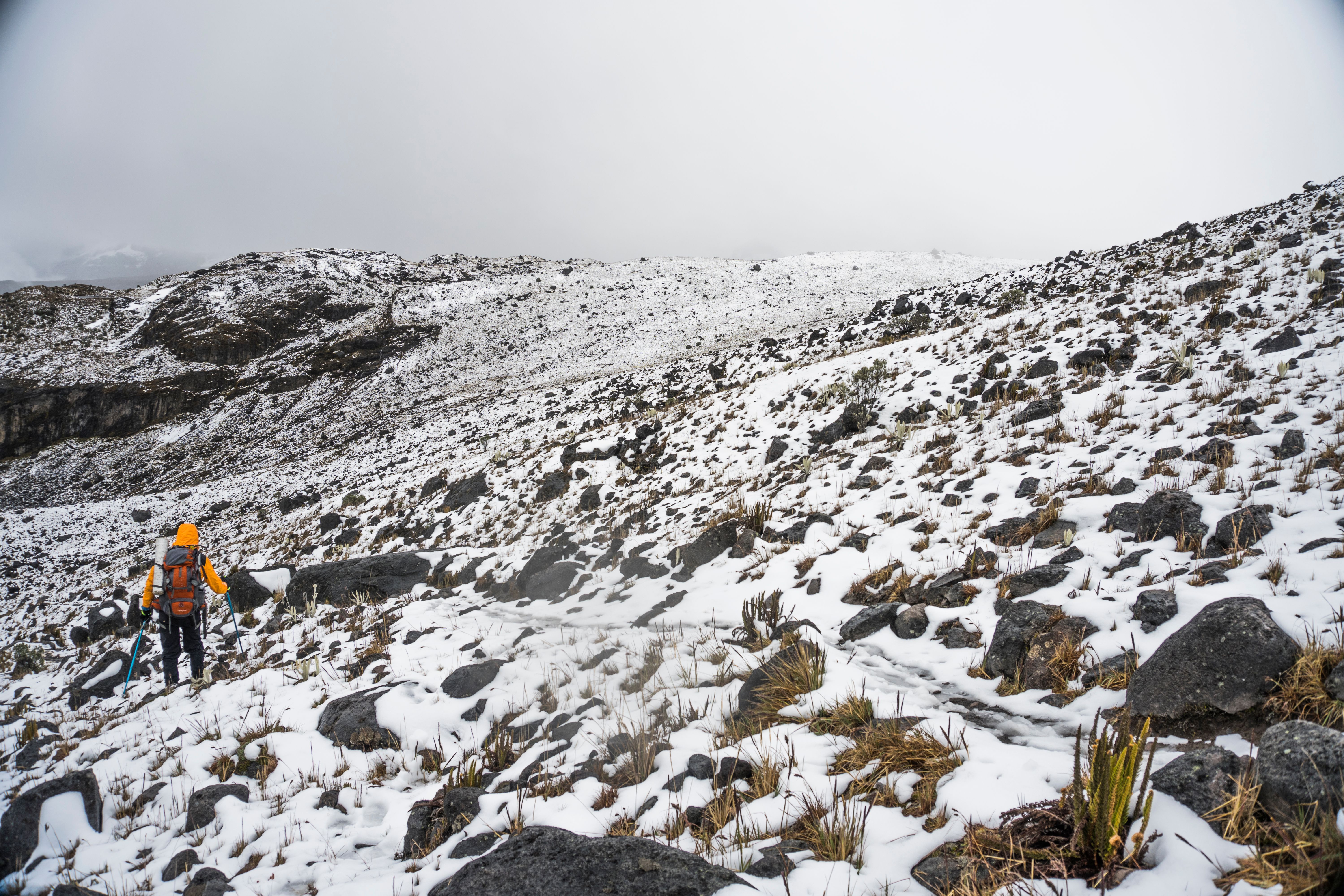 Breathtaking 9-Day Northern Circuit Kilimanjaro Climb with Expert Guides Review 2026 - Hiker clad in orange jacket trekking on snowy, rocky mountain slope with cloudy sky.