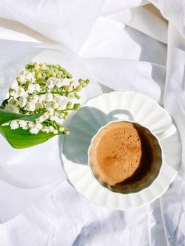 Top view of a coffee cup on a saucer with flowers on white textile.