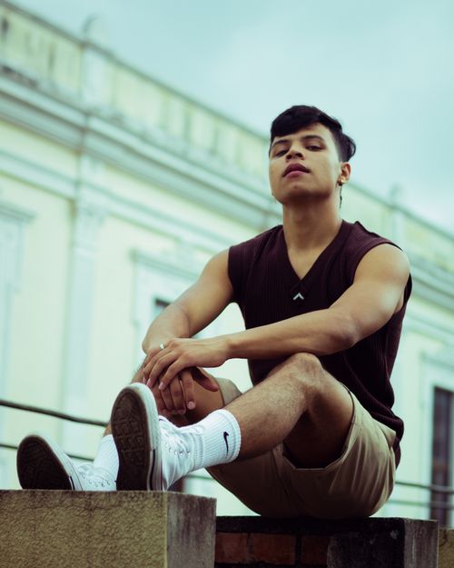 Free Young man sitting casually outdoors in summer attire. Vivid and relaxed vibe. Stock Photo