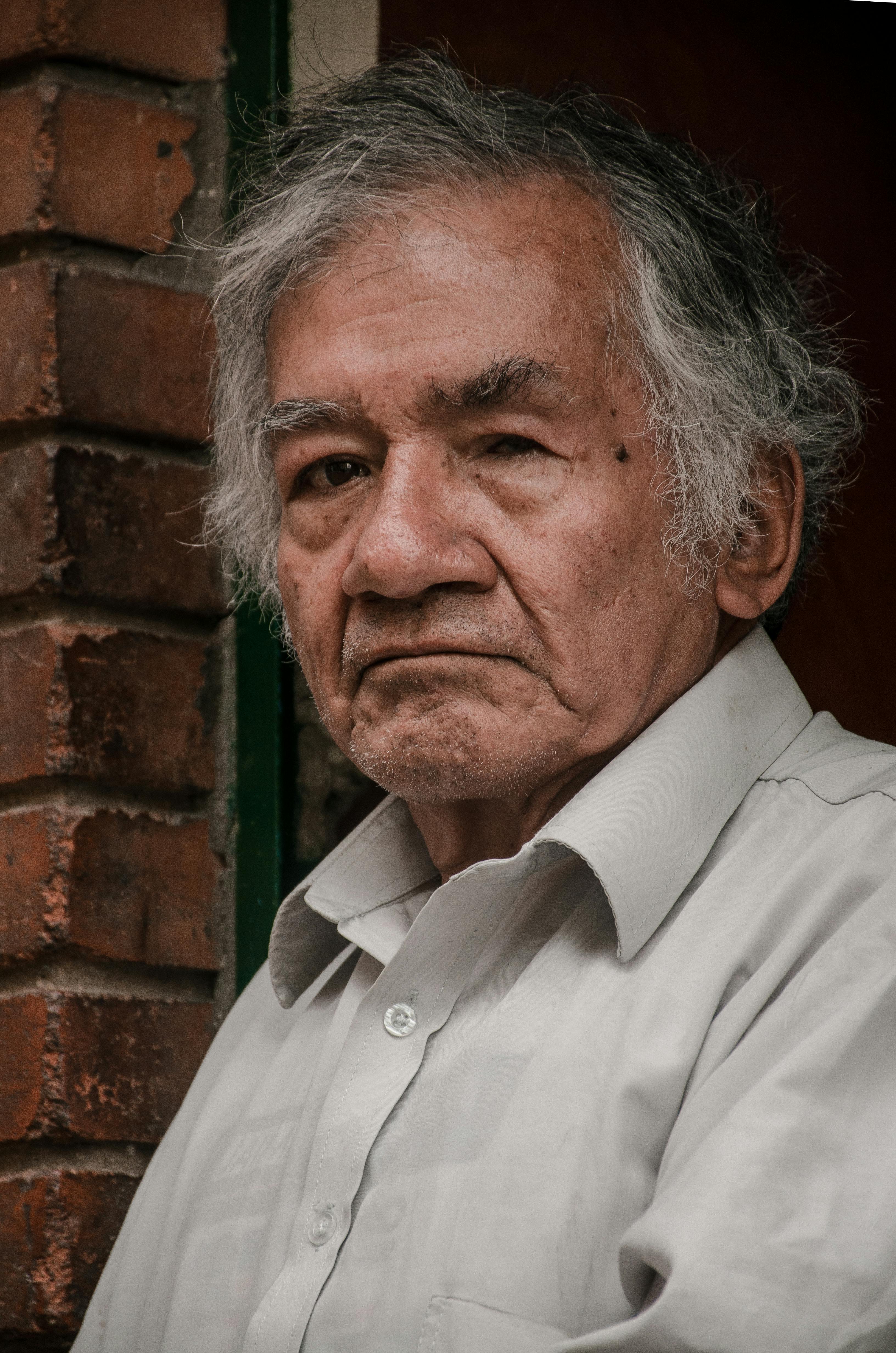 Close-up portrait of an elderly man with gray hair against a brick wall in Bogotá, Colombia.
