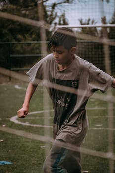 Wet young boy in gray shirt playing soccer in the rain on an outdoor field.