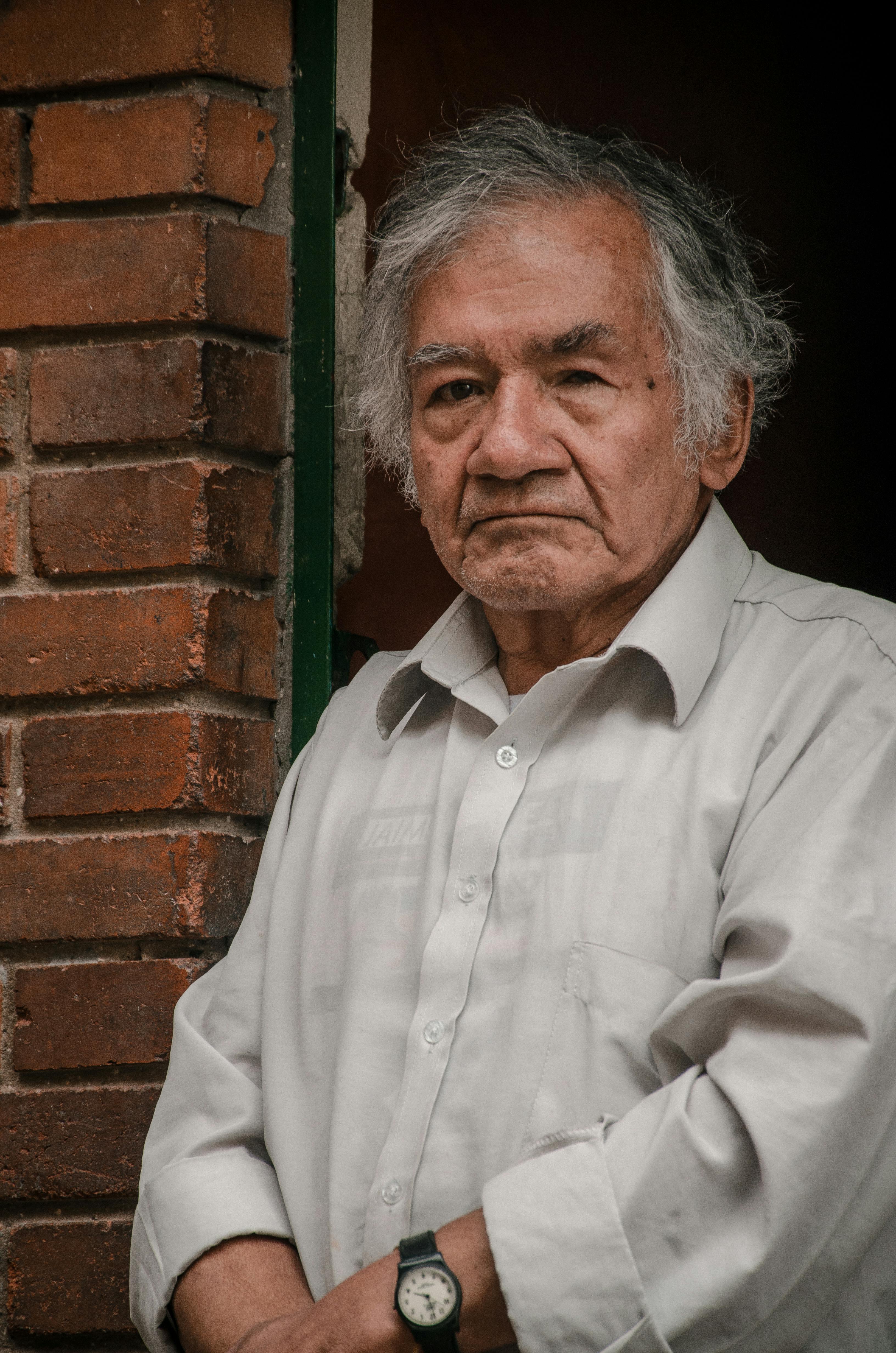 Portrait of an elderly man with gray hair standing by a brick wall in Bogotá, Colombia.