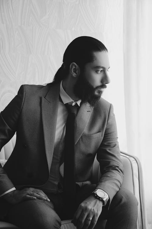 Black and White Photo of Man in Suit Sitting and Looking through the Window