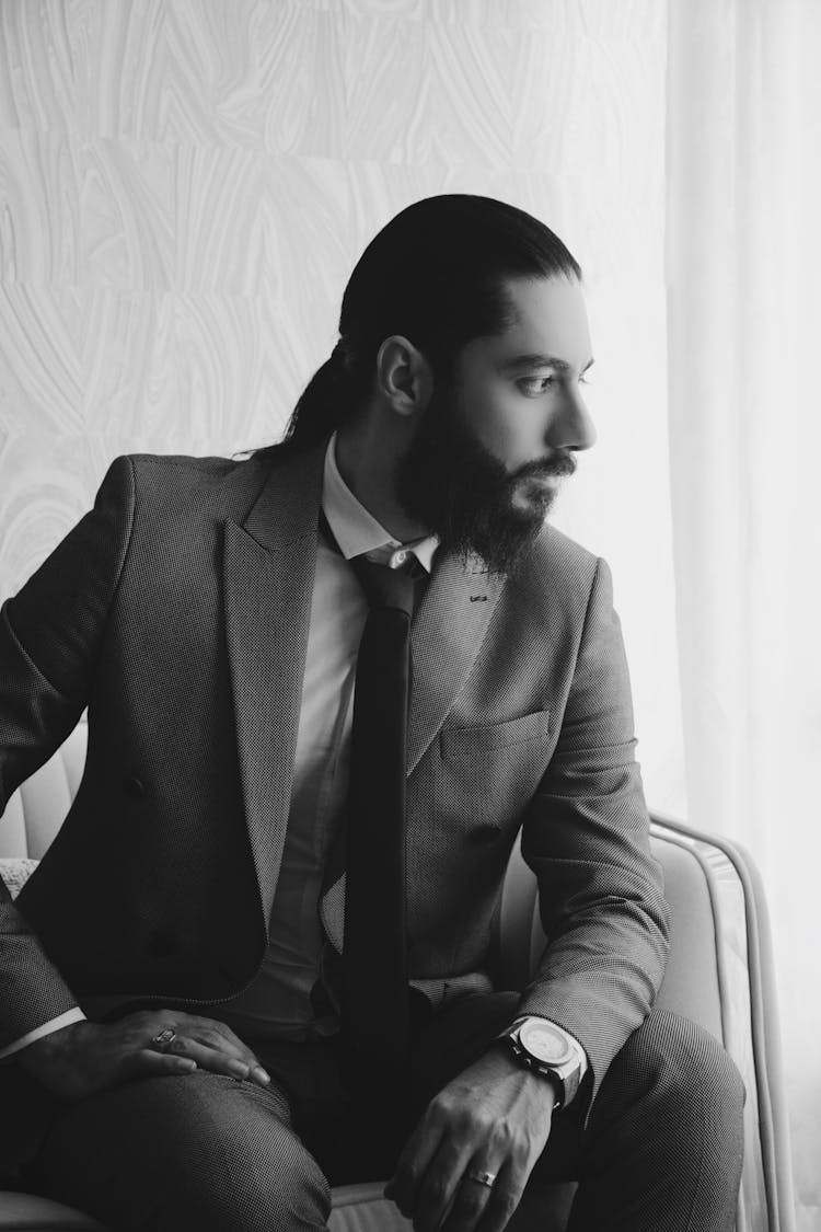 Black And White Photo Of Man In Suit Sitting And Looking Through The Window