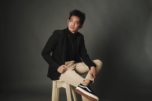 A Man in Black Long Sleeve Shirt and Brown Pants Sitting on White Wooden Seat