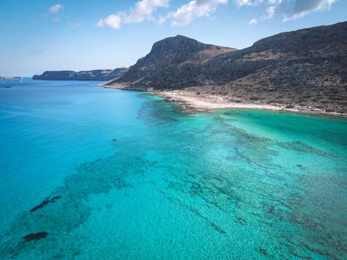 Brown Mountain Beside Blue Sea Under Blue Sky