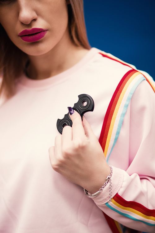 Free A trendy woman holds a fidget spinner against a vibrant blue background in a studio setting. Stock Photo