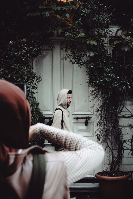 Street scene featuring a man in a hoodie and a woman in a hijab near a vine-covered door.