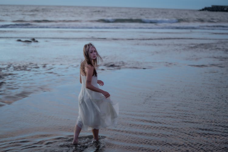 Woman In White Dress Walking On The Beach