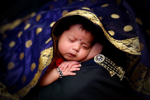 A cute baby peacefully sleeping under a beautifully designed traditional cloth, showcasing innocence and serenity.