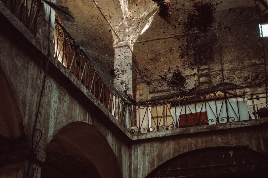 Weathered building interior with rusted iron balcony railing and water-damaged ceiling showing signs of long-term moistu