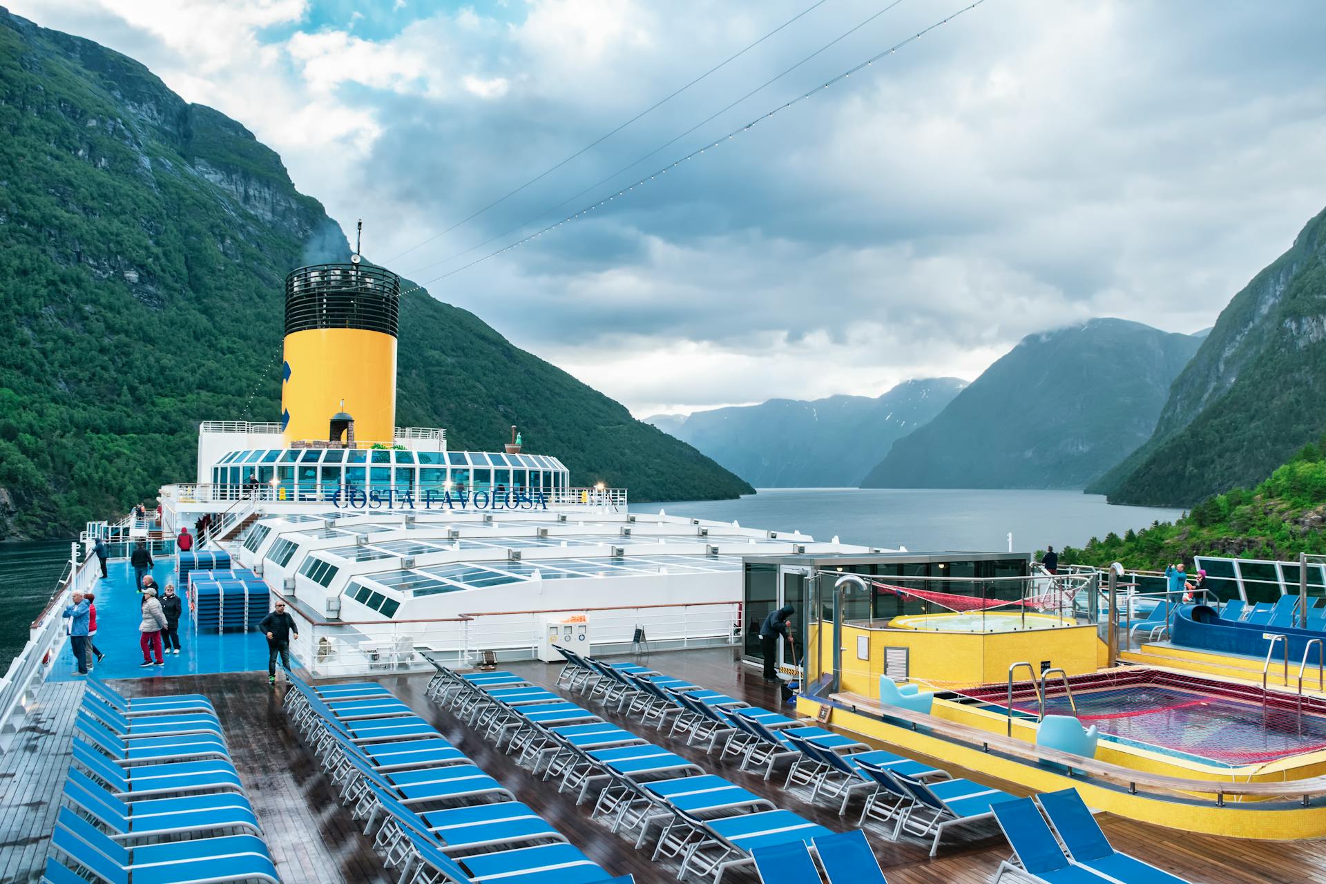 A luxurious cruise ship sailing through a stunning Norwegian fjord with scenic mountains and deck amenities.