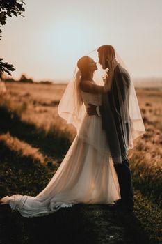 Bride and groom share a romantic moment at sunset in a scenic field.