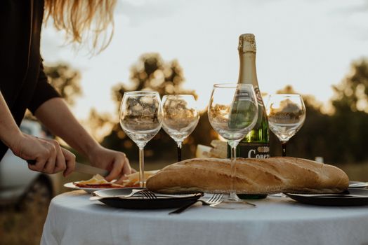Outdoor dining scene with baguette, champagne, and wine glasses on a neatly set table.