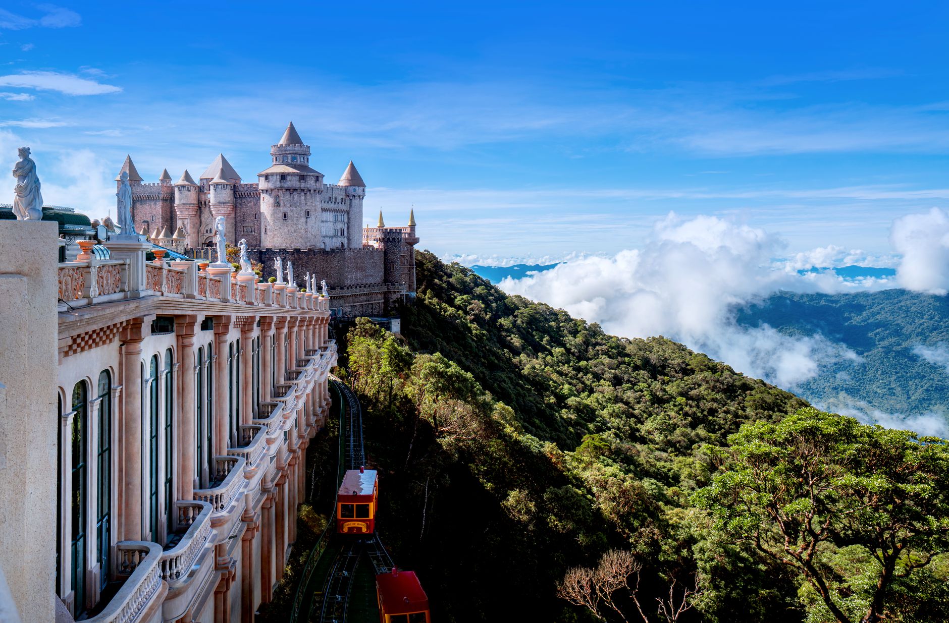 Majestic castle on a mountain summit with panoramic forest views under a clear blue sky.