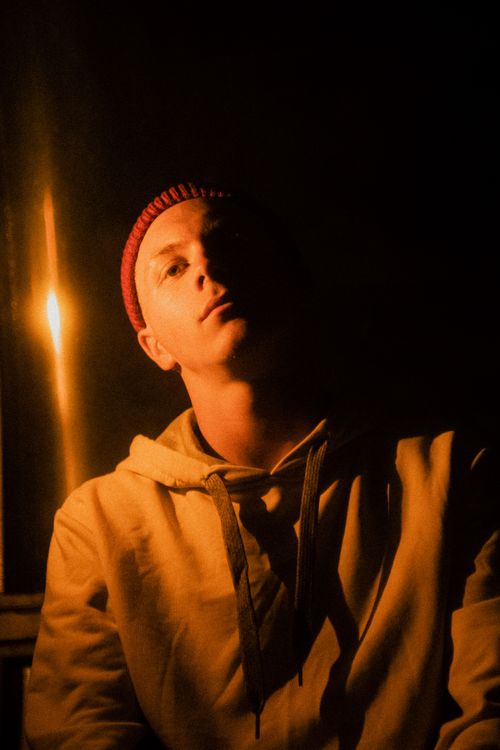 Free A pensive young man lit by warm candlelight wearing a red beanie and hoodie. Stock Photo