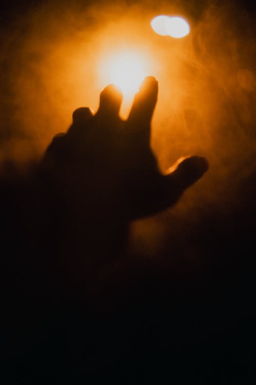 Close-up of Person Hand Stretching to Light in Dark