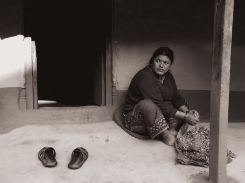 Free Black and white image of a woman sitting on a doorstep with sandals nearby. Stock Photo