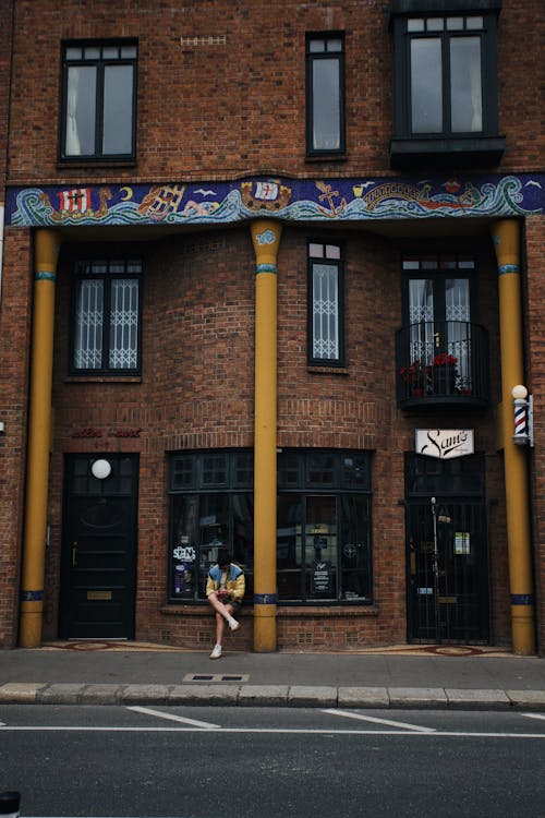 A Person Sitting on a Brown Bricked Building with Yellow Concrete Pillars