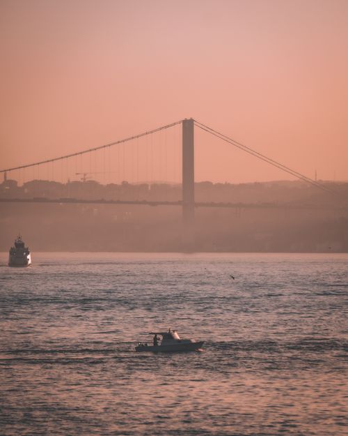 Free Serene sunset view of boats sailing near the iconic Bosphorus Bridge in Istanbul, Turkey. Stock Photo