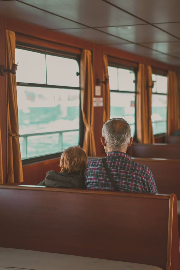 Back View Of An Elderly Couple Sitting On The Wooden Bench Inside A Train