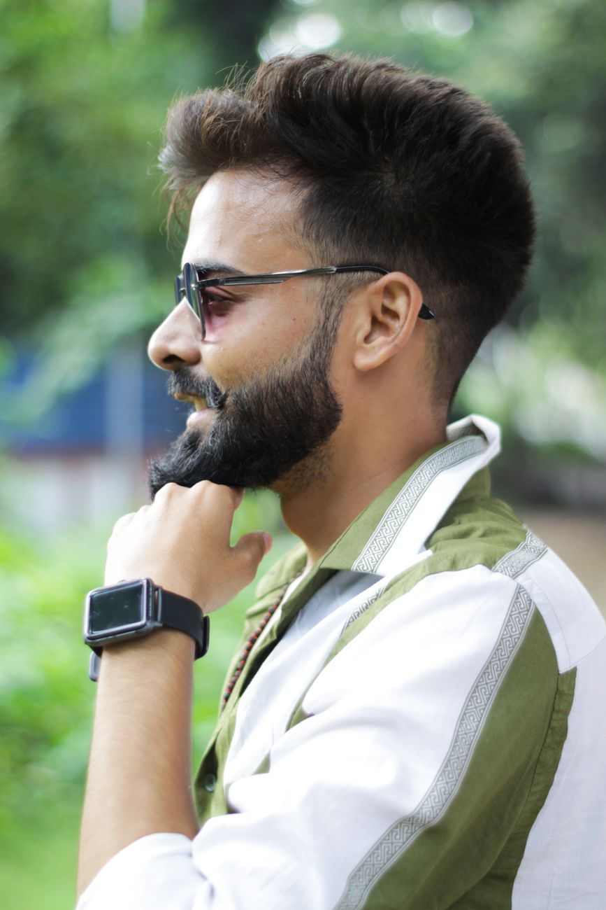 Profile of a young man with a beard and sunglasses, contemplating in a lush park.