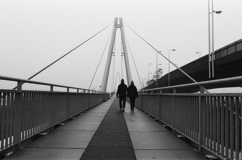 Free Monochrome image of a couple walking on a contemporary bridge in a minimalist urban setting. Stock Photo