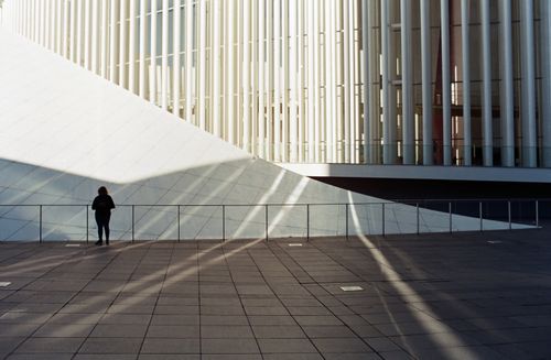 Free Silhouetted person stands before modern architectural facade with striking shadows. Stock Photo