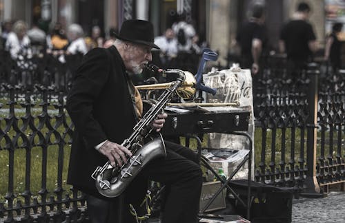 Free Man Sitting on Stool While Playing Saxophone Beside Fence Stock Photo
