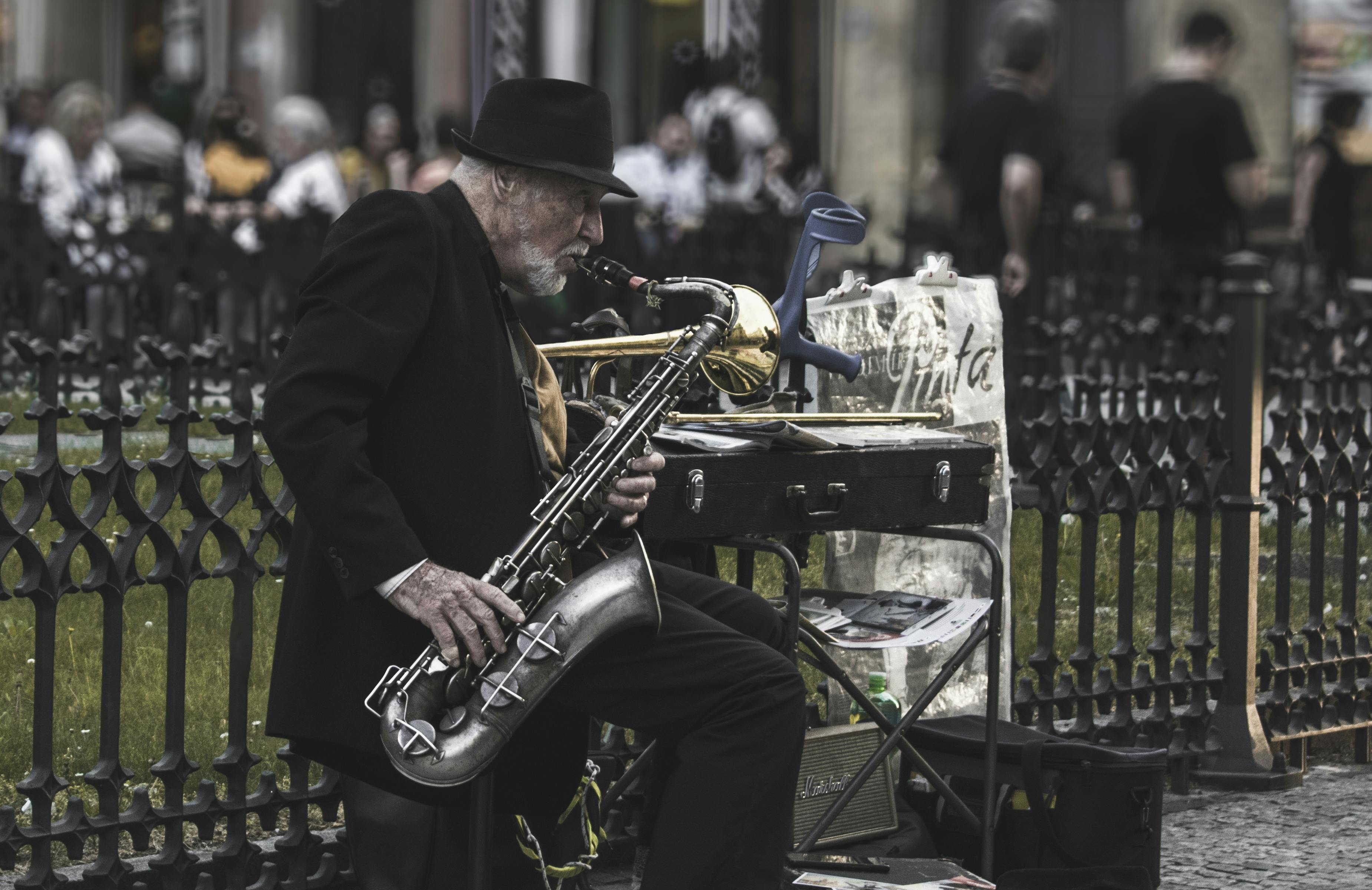 Hombre Sentado En Un Taburete Mientras Toca El Saxofón Junto A La Valla ...
