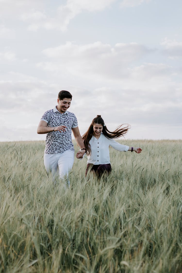 Couple Running Through Field Holding Hands