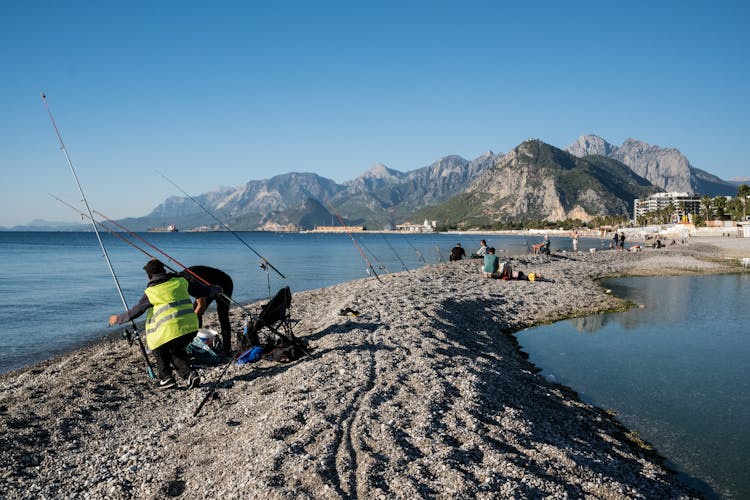 A Group Of People Fishing On A Beach Near A Mountain