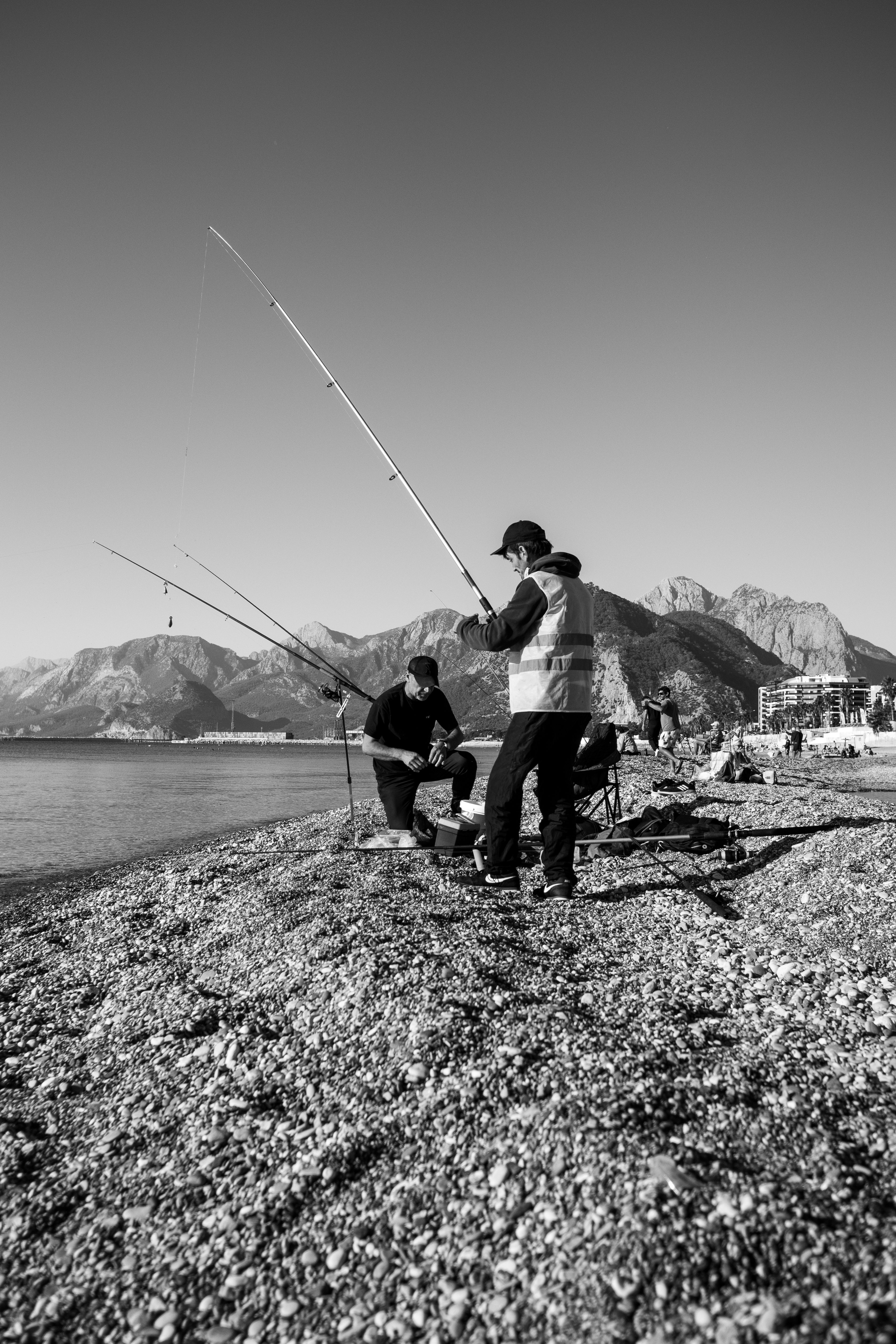 A Grayscale Photo of a pair of People Fishing on a Beach Near a ...