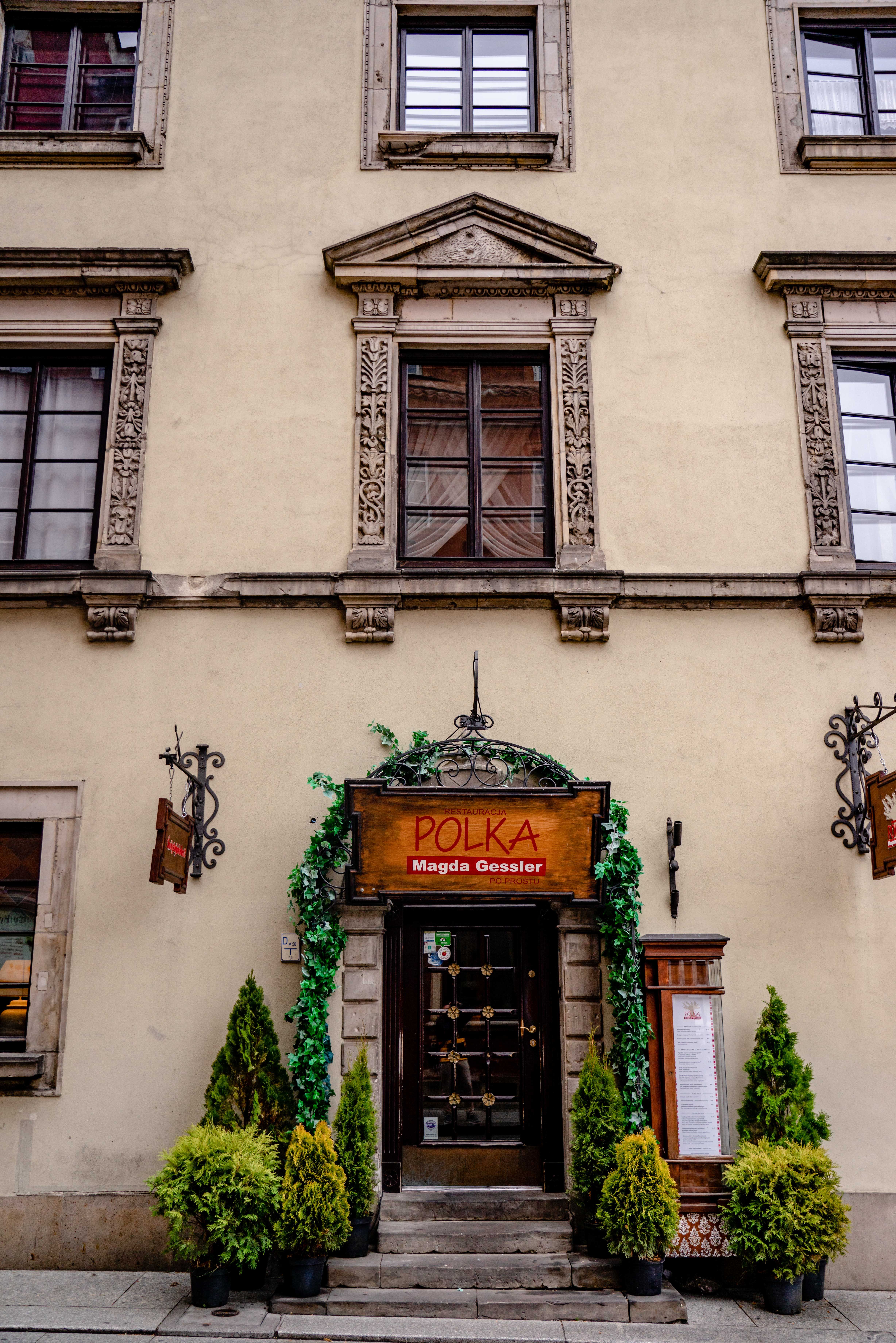 Charming restaurant entrance on a historic street in Warsaw, Poland, adorned with greenery.