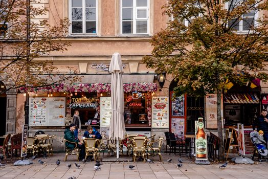 Outdoor café scene in Warsaw, Poland with people, pigeons, and a cozy atmosphere.