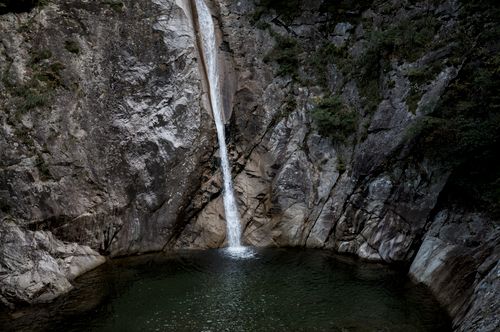 Free A tranquil waterfall descends over rugged rocks into a serene pool, surrounded by nature. Stock Photo