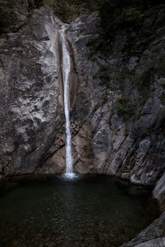 A serene waterfall cascades down rugged rocks into a tranquil pool, showcasing nature's beauty.